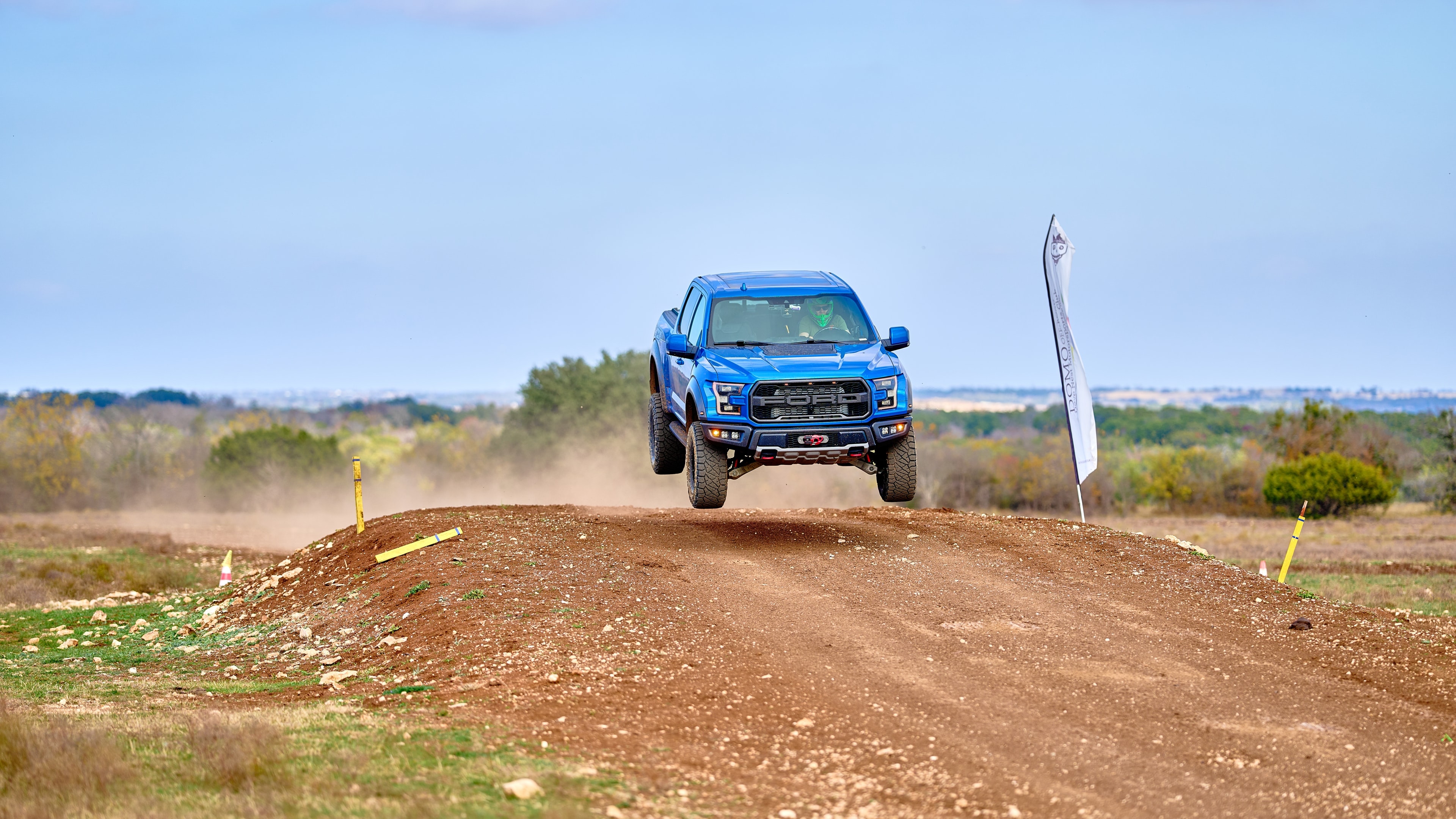 Ford Raptor jumping dirt ramp — open landscape